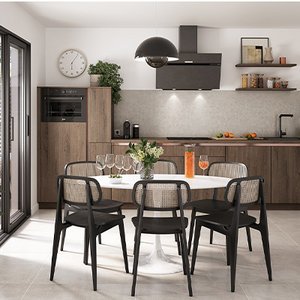 la cuisine Luna d’ixina une cuisine de style industriel, aux murs blancs avec placards en bois foncé, aux accents en métal noir. Au premier plan, une table et des chaises noires avec empiècement en rotin clair. La décoration est minimaliste, avec quelques plantes vertes et des étagères ouvertes sur lesquelles figurent des bocaux en verre.